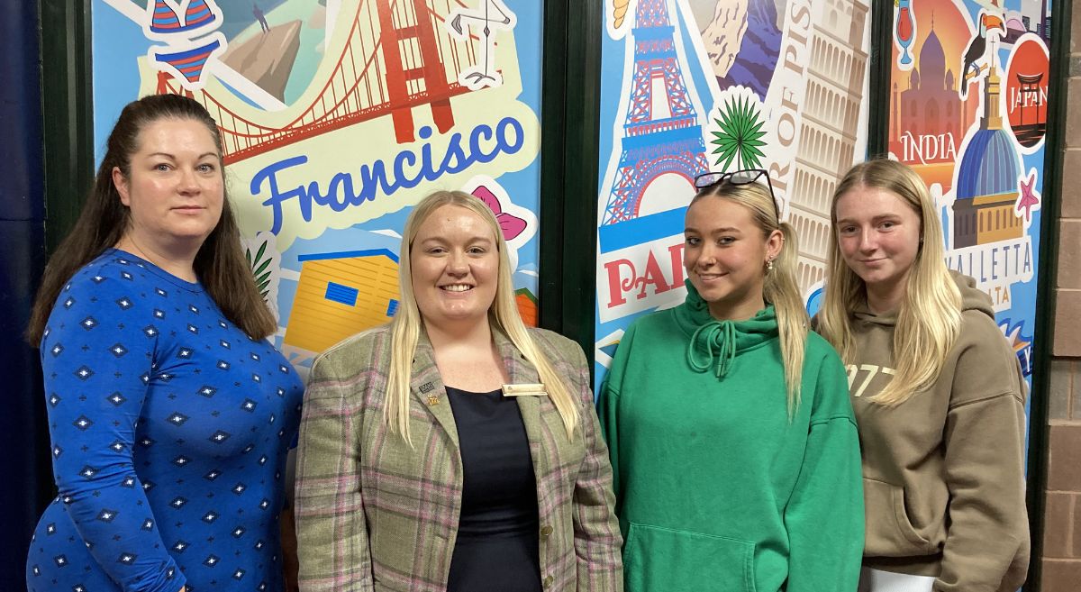 Four females pictuted in front of holiday graphic featuring famous world landmarks